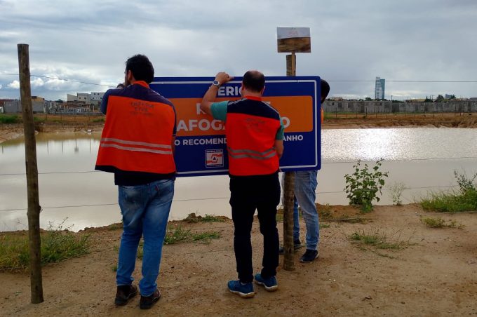 Defesa Civil instala placas no entorno da bacia de contenção do Vila América com alerta para risco de afogamento